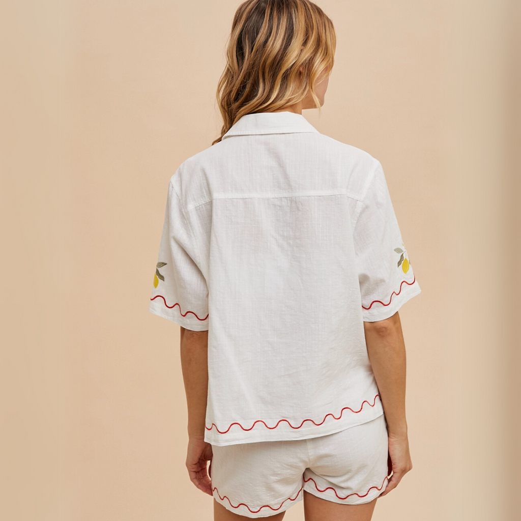 Close-up of embroidered fruit and florals on scalloped button-up top.