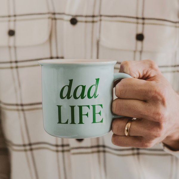 Person in plaid shirt holding a mint green “Dad Life” ceramic mug

