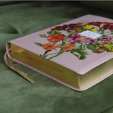 “Artisan Bible pink edition on green couch with gold gilded pages”

