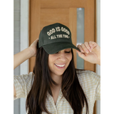 Close-up of deep green embroidered 'God Is Good All the Time' trucker hat, showing the structured fit and bold lettering.