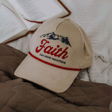 "Beige corduroy 'Faith Can Move Mountains' hat resting on a quilt with an open Bible, emphasizing faith and inspiration."

