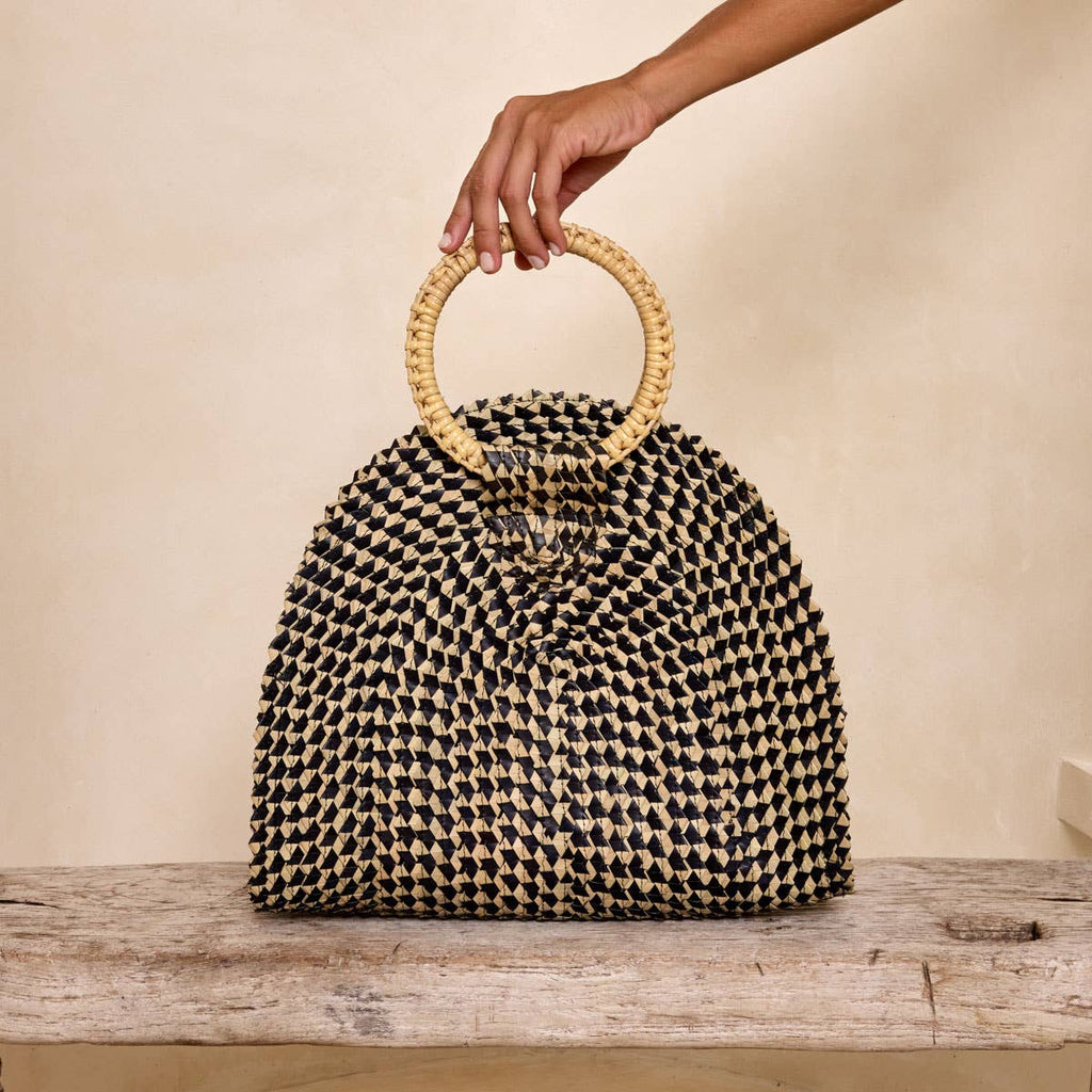 Woven handbag with wooden handle held by a hand on a wooden surface.
