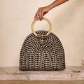 Woven handbag with wooden handle held by a hand on a wooden surface.
