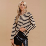 Woman wearing a boat neckline striped knit pullover sweater with long sleeves, styled with a leather skirt against a beige background.