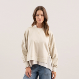 Front view of a beige washed knit top featuring a crewneck design and extended shoulder seams, styled with denim.