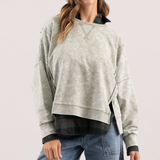 Model wearing a washed knit crewneck top with patchwork detailing and long sleeves, layered over a plaid shirt, paired with jeans.