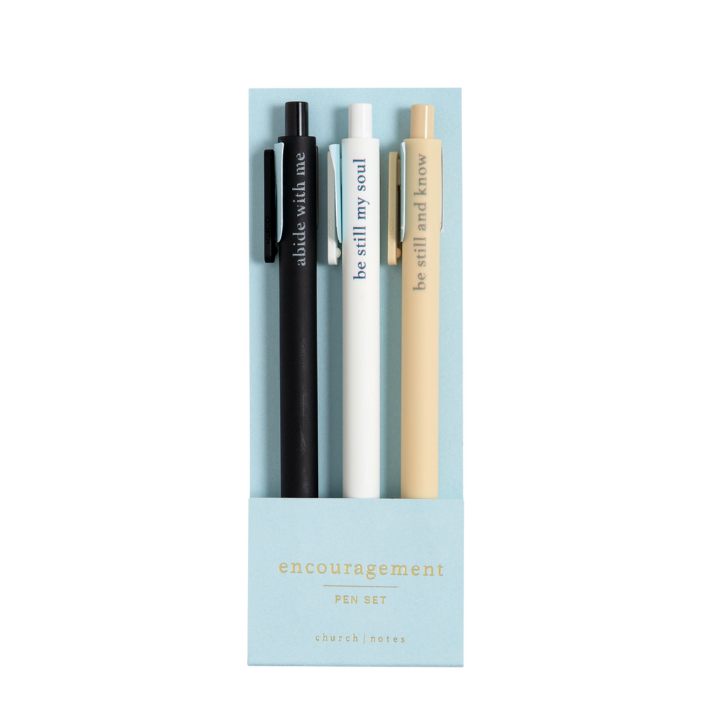 Faith-based pens writing spiritual phrases in ink, laid out on a flat-lay with a notepad.

