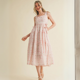 Woman wearing pink floral ruffle strap midi dress with side bows and tiered skirt


