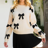 Feminine cream knit sweater with black bow accents styled with a flowy black skirt, perfect for a casual yet elegant outfit.