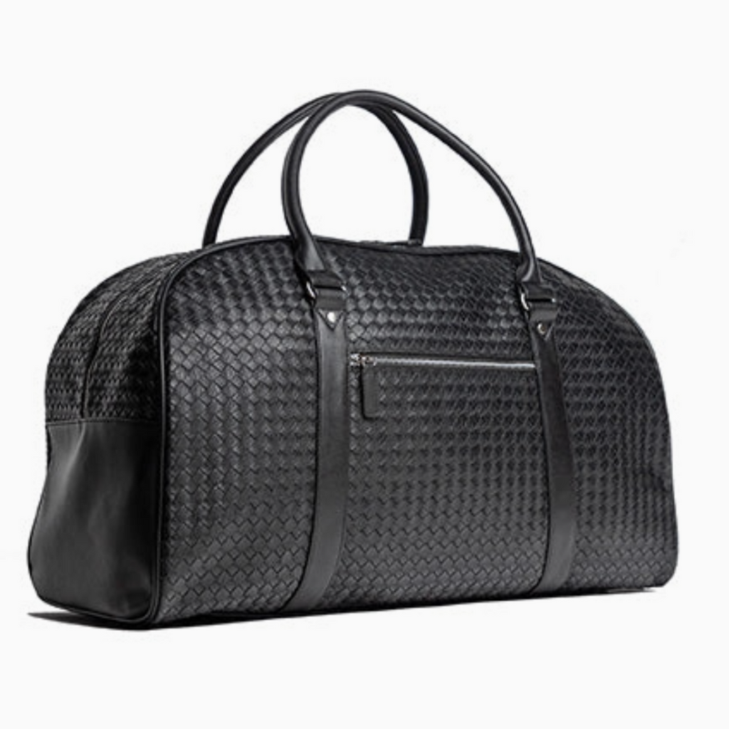 Angled view of luxury woven leather weekender bag with top handles and spacious design for travel essentials.
