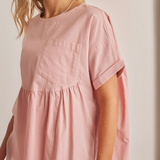 Close-up of pocket, sleeve, and neckline details on blush pink cotton peplum top.
