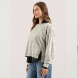 Back view of a washed knit top in beige, highlighting extended shoulders and relaxed fit, layered over a striped shirt.