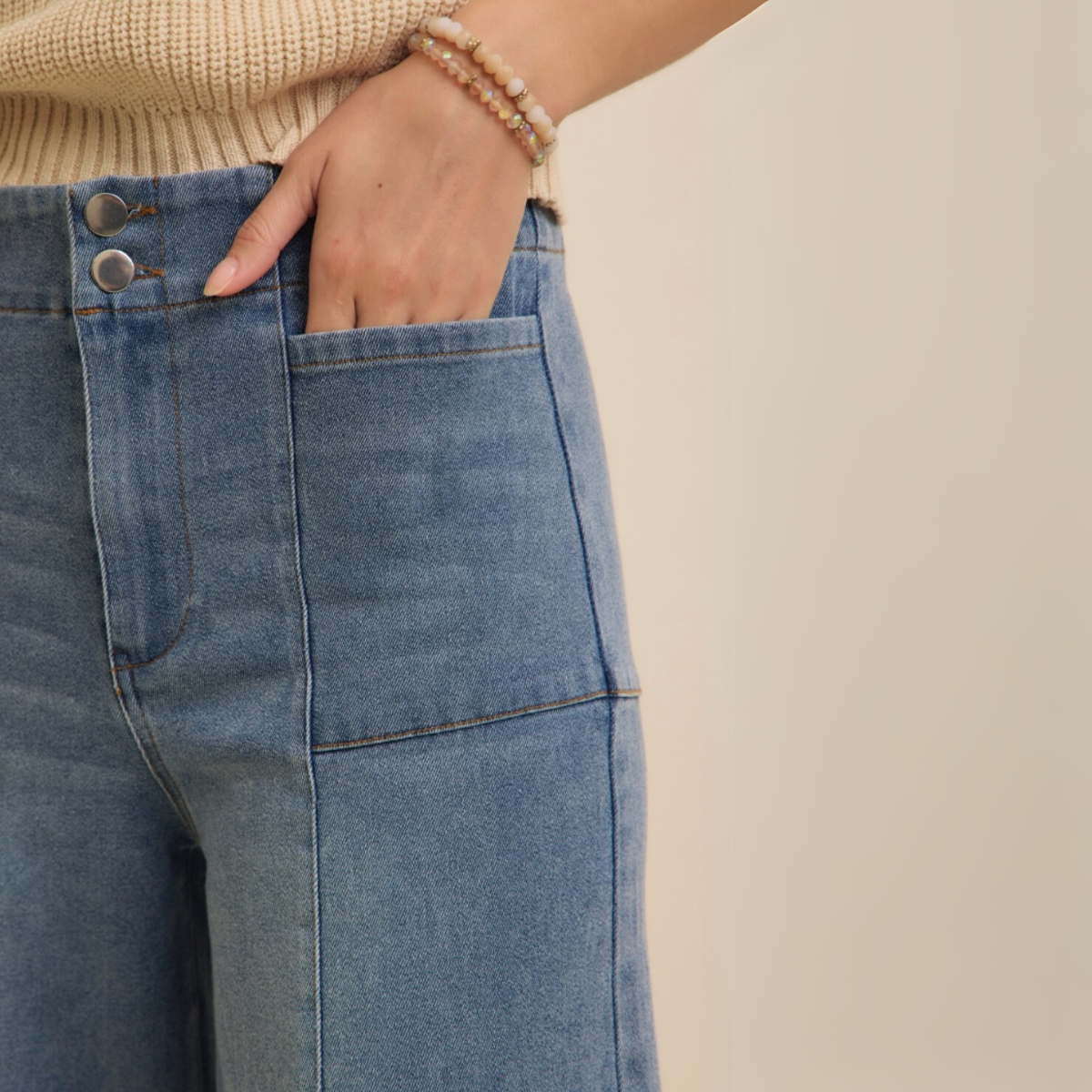 Close-up of front pocket and waistband with double button closure on denim jeans.
