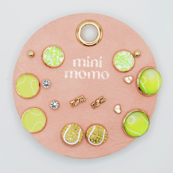 Mini Momo Tennis Earring Set featuring green and gold-tone tennis-themed stud earrings displayed on a pink round leather card.