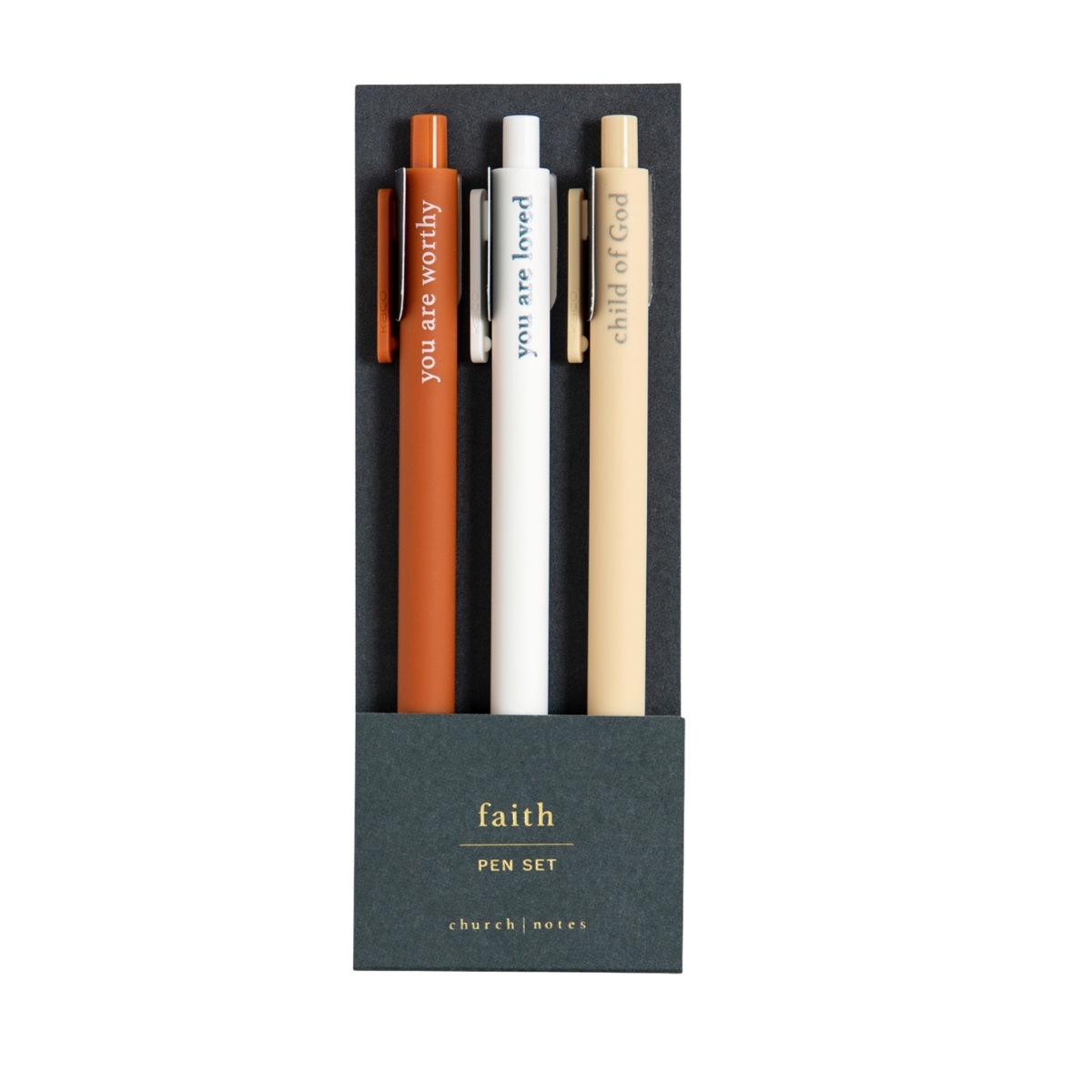 Faith-based pens writing spiritual phrases in ink, laid out on a flat-lay with a notepad.

