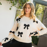 Close-up of a chic cream sweater featuring bold black bow embellishments on the sleeves and front.