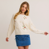 Full view of the Strawberry Embellished Knit Sweater paired with a denim skirt, showcasing its relaxed fit and whimsical details.