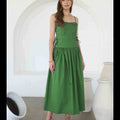 Woman wearing a green dress standing in a minimalistic room with white arches and vases.