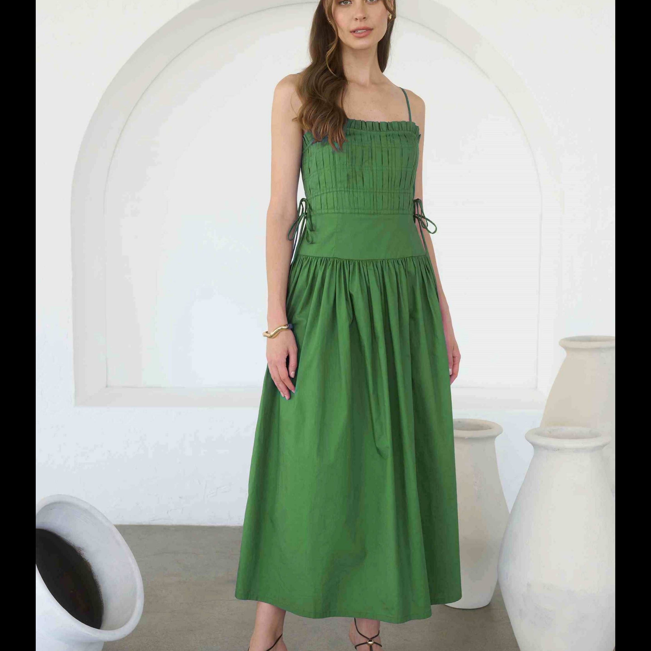 Woman wearing a green dress standing in a minimalistic room with white arches and vases.