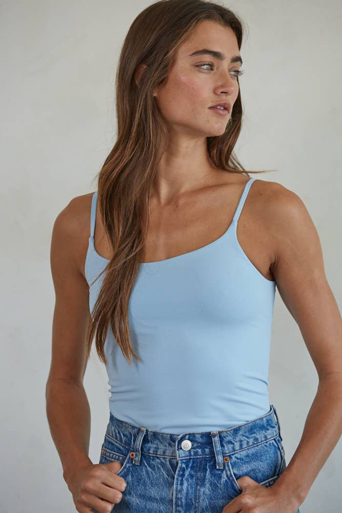 Woman wearing a light blue tank top and blue jeans against a plain background