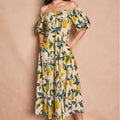 Woman wearing a off-shoulder dress with lemon print against a beige background
