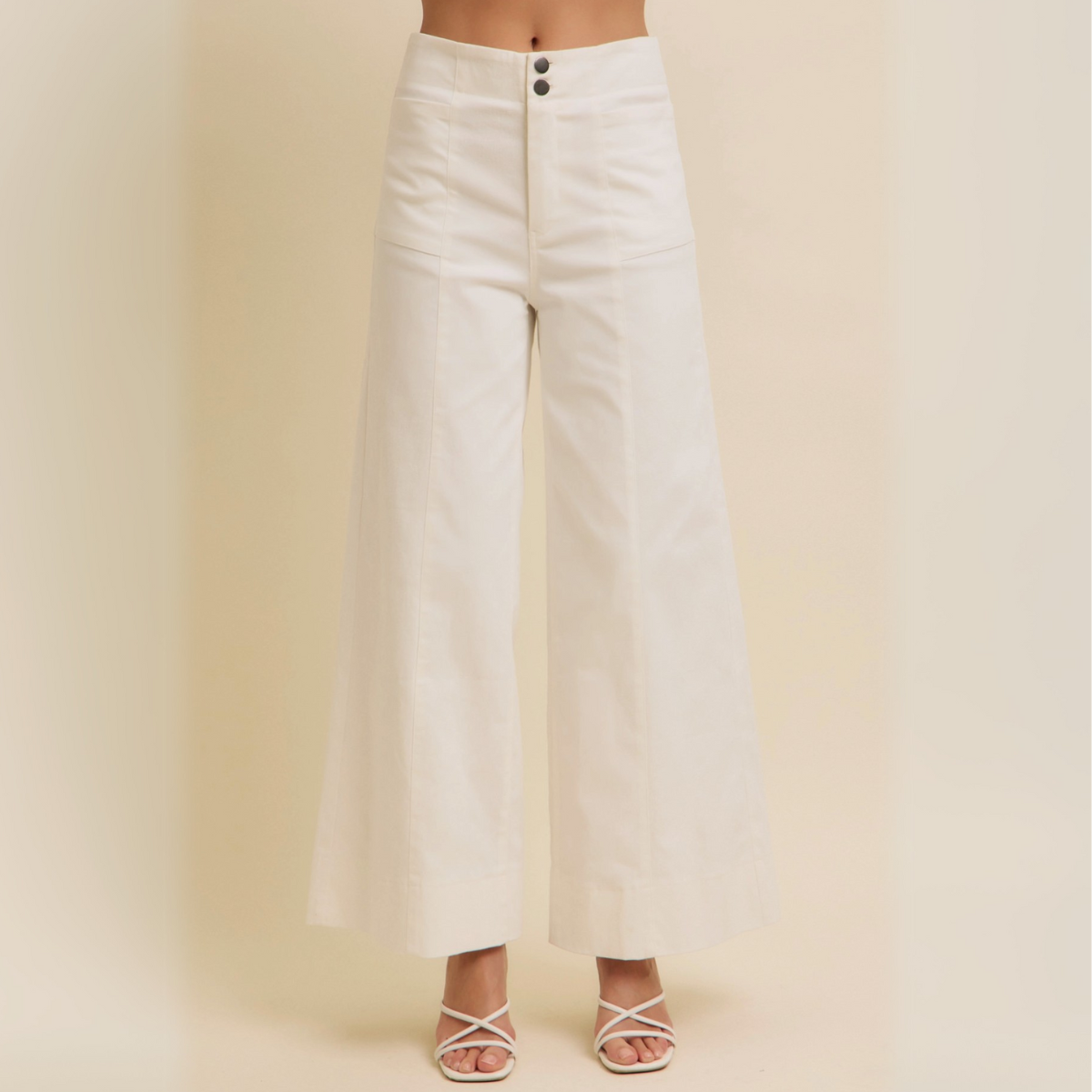 Front view of white high-rise wide-leg cotton twill pants with double-button waist and full-length hem, styled with heeled sandals.

