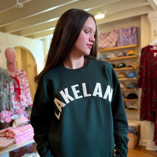 Woman wearing a green sweatshirt with 'LAKELAND' printed on it in a store setting.