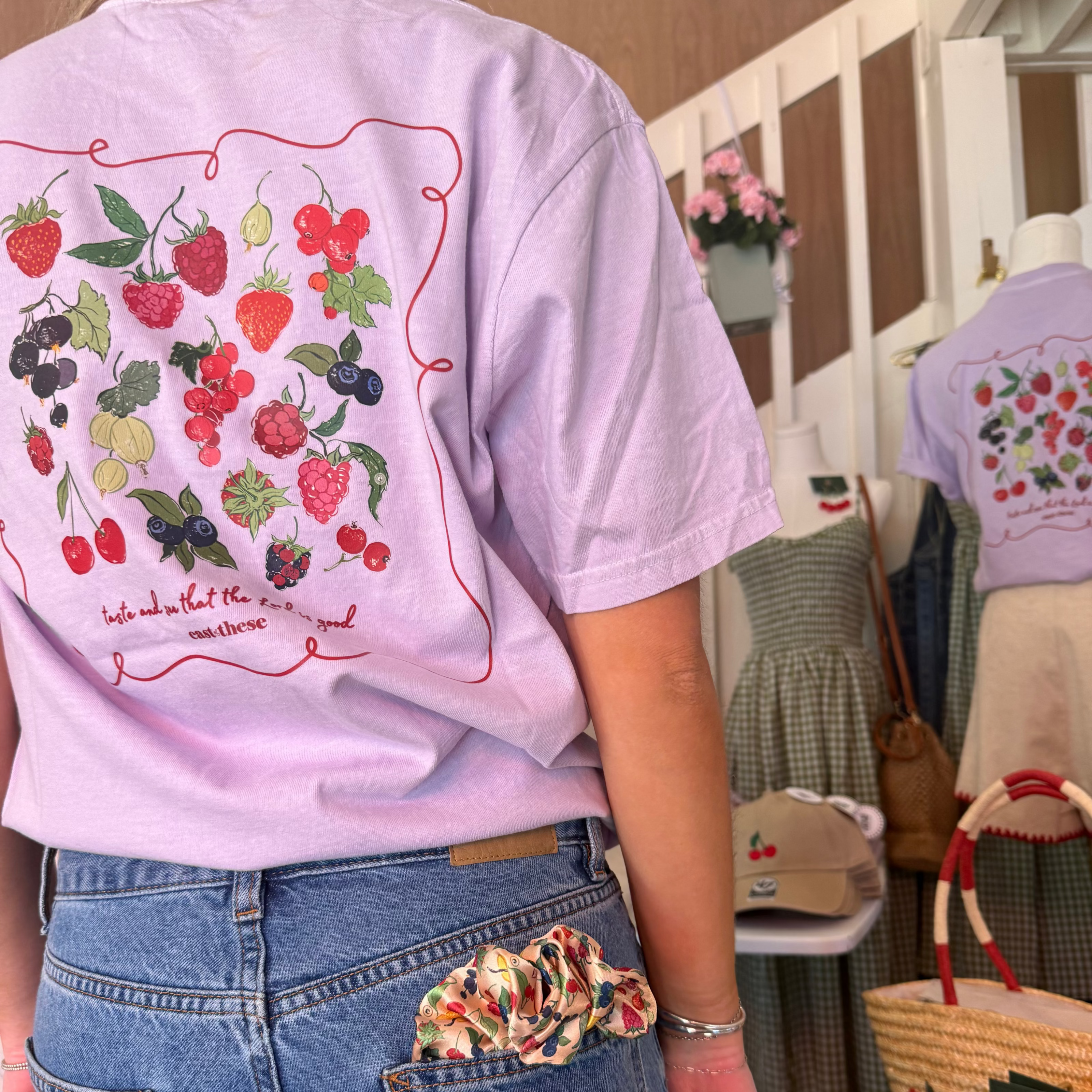 Person wearing a light purple t-shirt with fruit illustrations in a store setting.