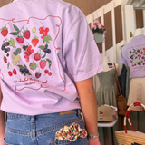 Person wearing a light purple t-shirt with fruit illustrations in a store setting.