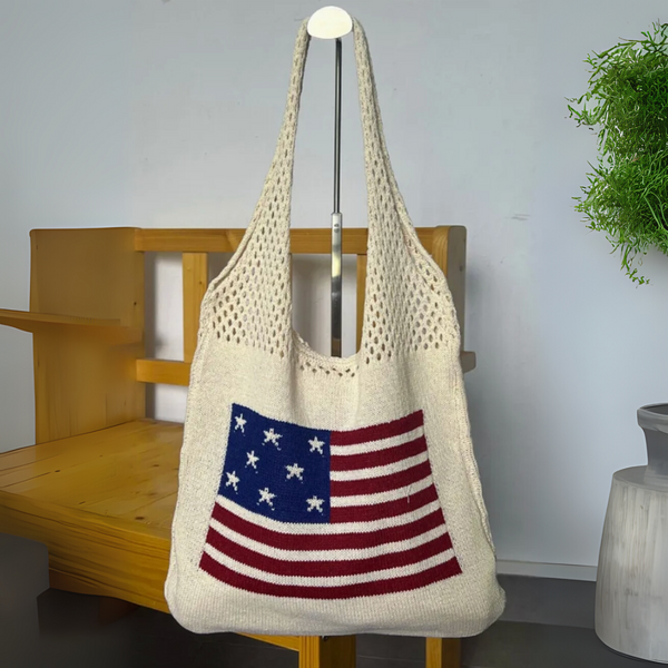 Beige knit tote bag with an American flag pattern hanging on a wooden chair indoors.

