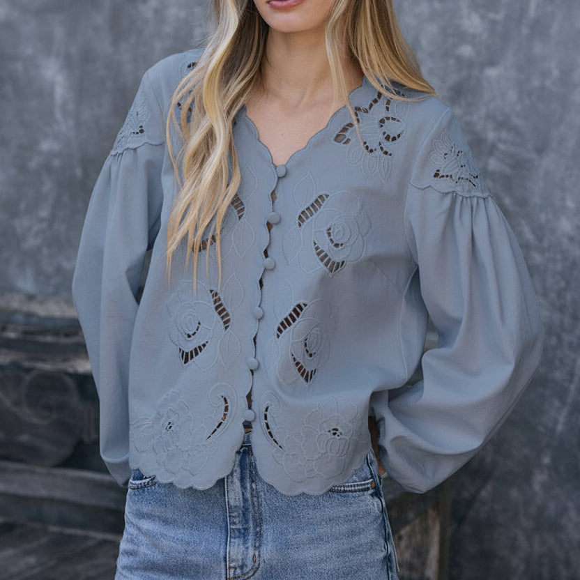 Woman wearing a white blouse with lace details and blue jeans against a gray background
