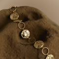 Gold belt with circular pendants on a brown fabric background in Lakeland, Florida women's fashion boutique. 