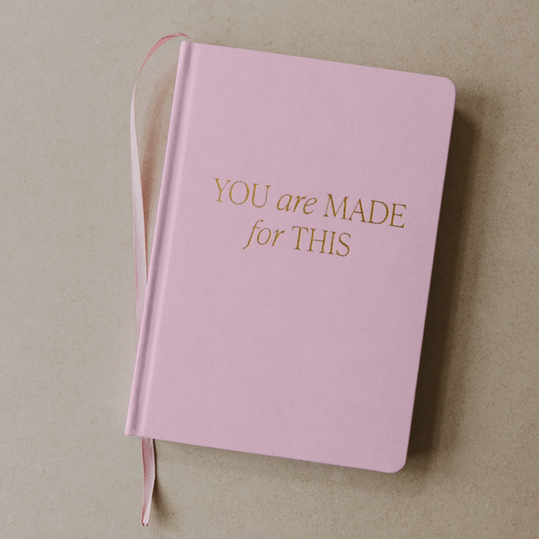 Pink hardcover journal with gold foil text reading “You Are Made for This” and satin ribbon bookmark – angled top-down view.

