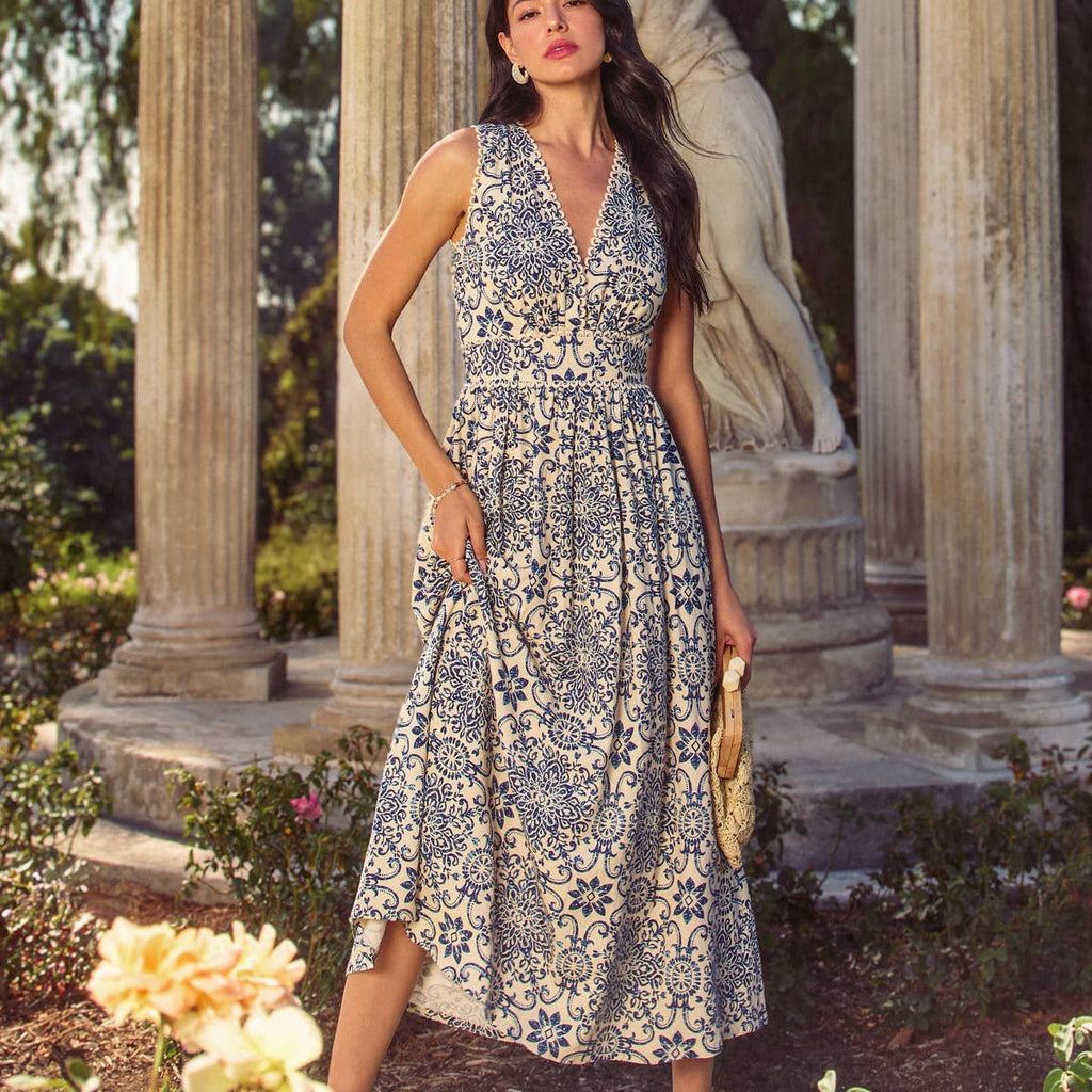 Woman in a floral dress standing in a garden with classical columns and statues.