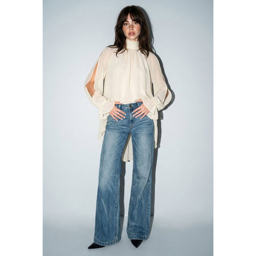 Woman wearing a cream blouse and blue jeans against a plain background
