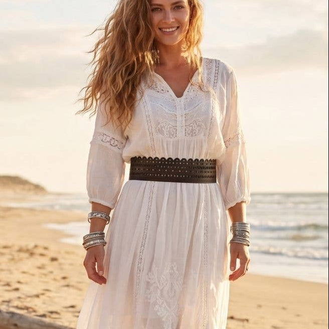 Woman in a white dress standing on a beach with a sunset in the background