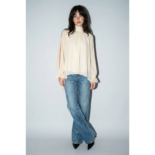 Woman wearing a cream blouse and blue jeans against a white background